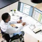 Man in wheel chair working with spreadsheets on two screens.