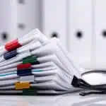 stack of paperwork on desk next to glasses.